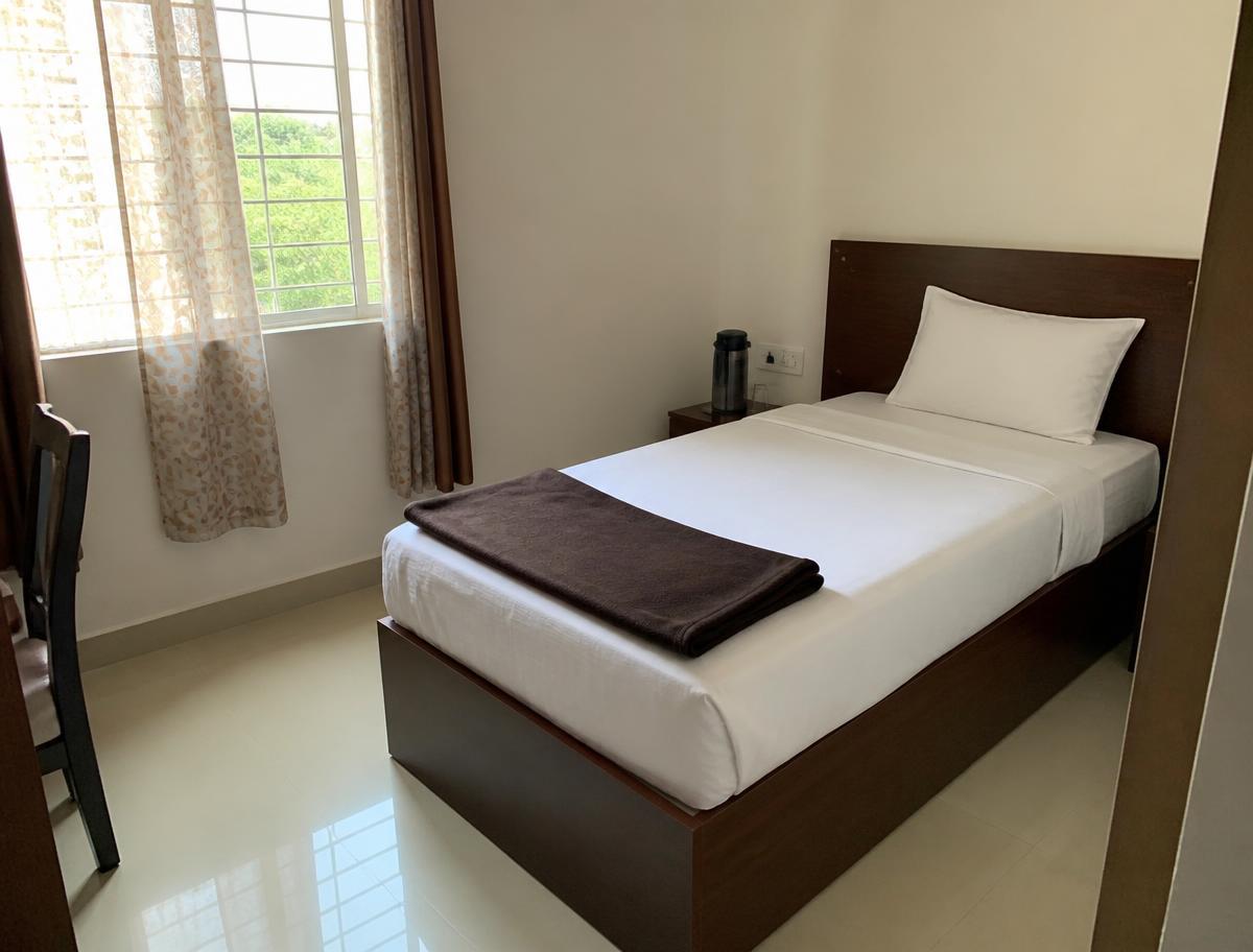 Illustrative photograph of a small, simply furnished bedroom with a single bed and a curtained window